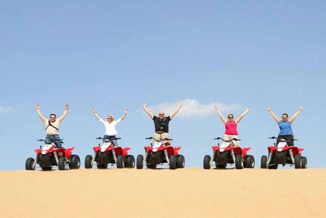Quad biking adventure across golden sand dunes in Marsa Alam desert under a clear sky